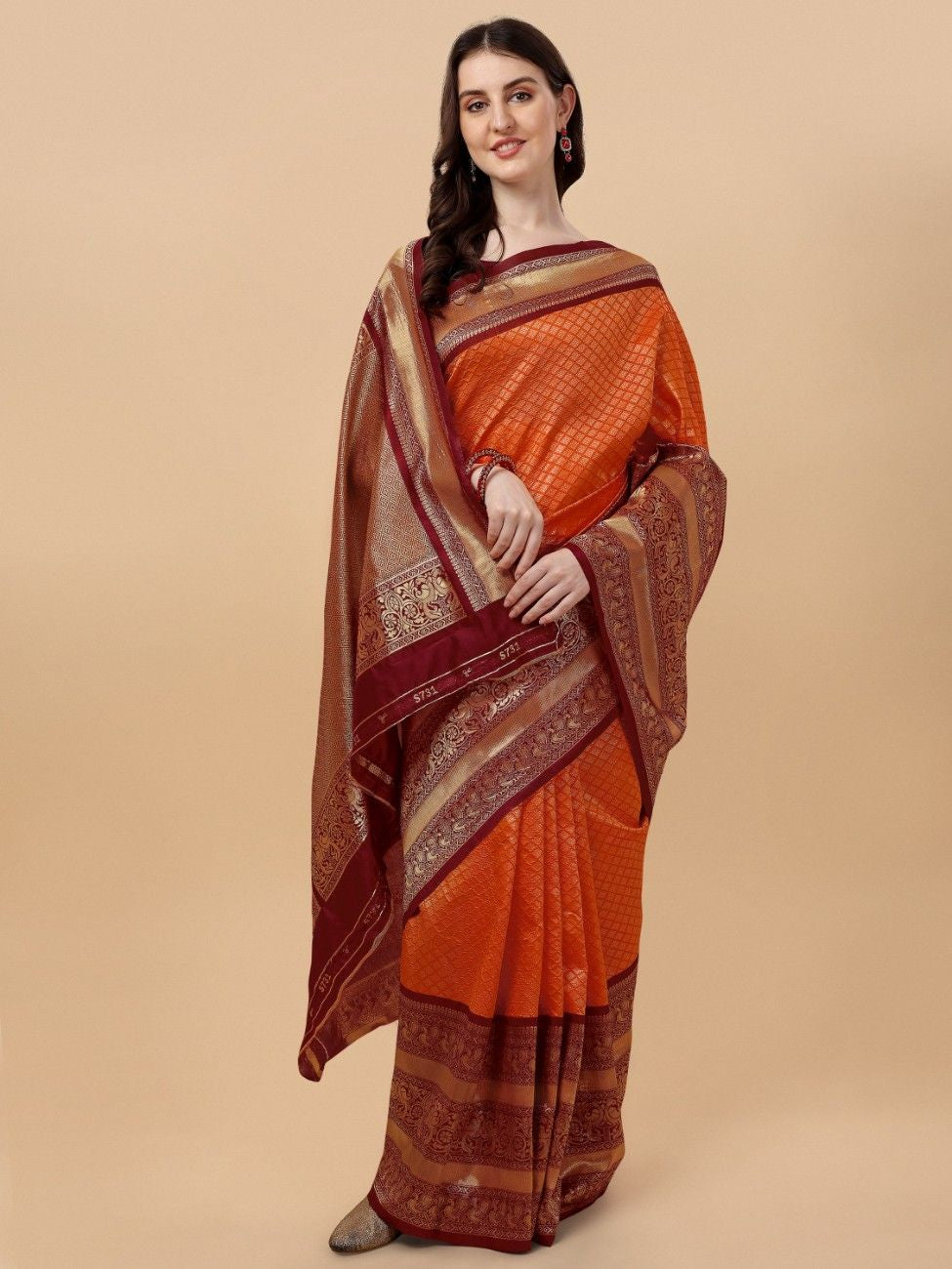 Woman wearing an orange and brown saree with a beige background
