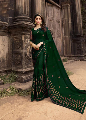 Woman in a green saree with black patterns standing in front of stone architectural elements.