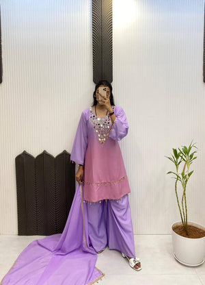 Person wearing a traditional outfit with a pink top and purple pants, standing indoors.