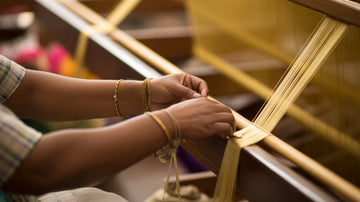 Indian artisans weaving pure silk saree on a traditional handloom with golden zari threads — craftsmanship at Maharani Weaves.
