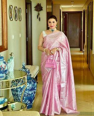 Woman in a pink saree standing in a hallway with decorative vases and wall art.