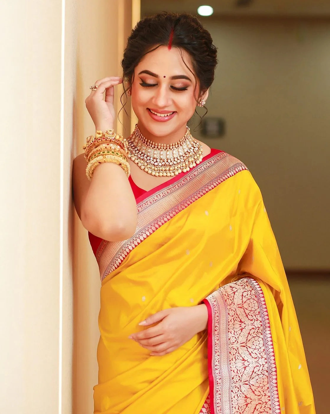 Woman in a yellow saree with jewelry indoors
