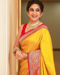 Woman in a yellow saree with red blouse and gold jewelry, smiling.