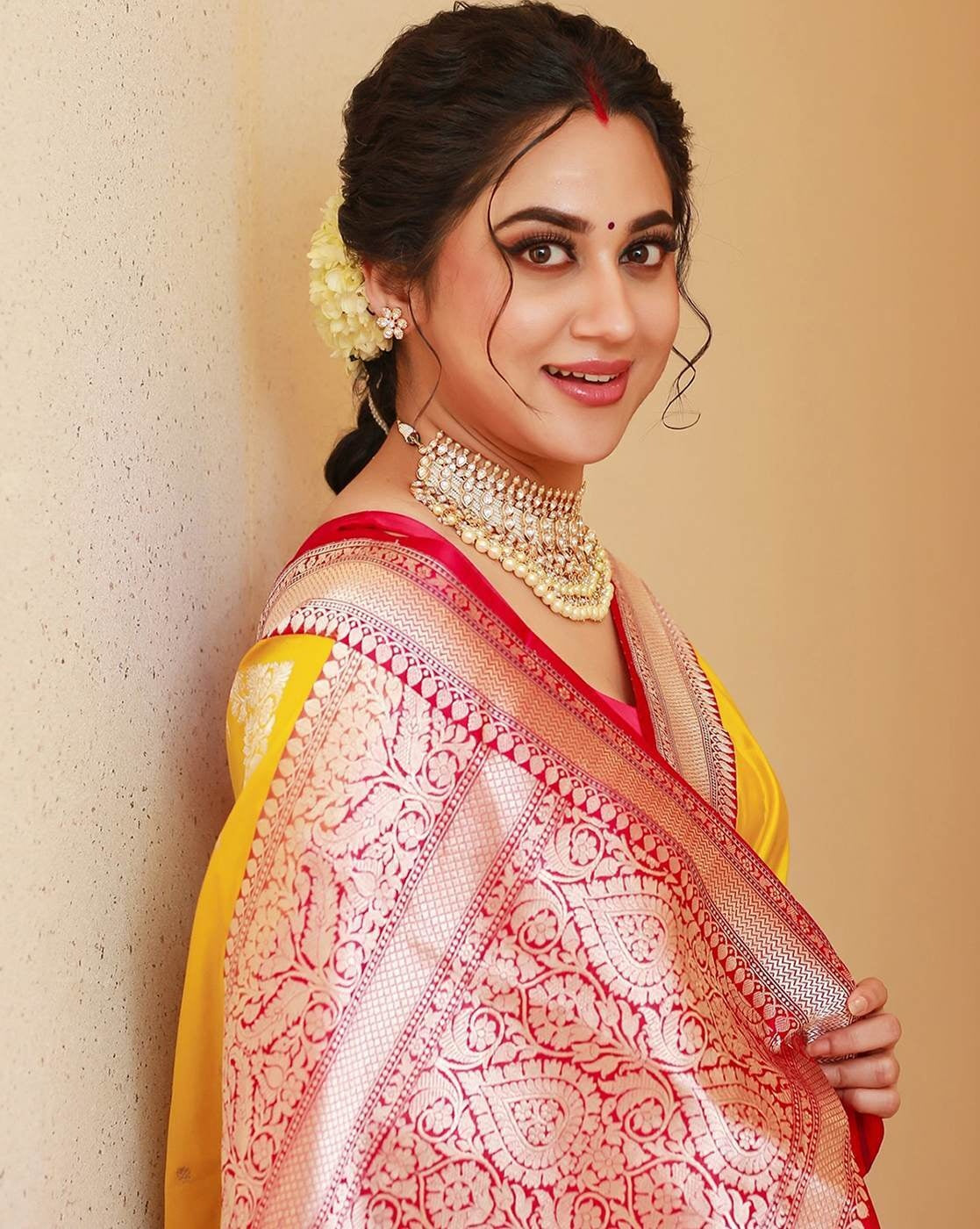 Woman in a yellow and red saree with jewelry against a beige background