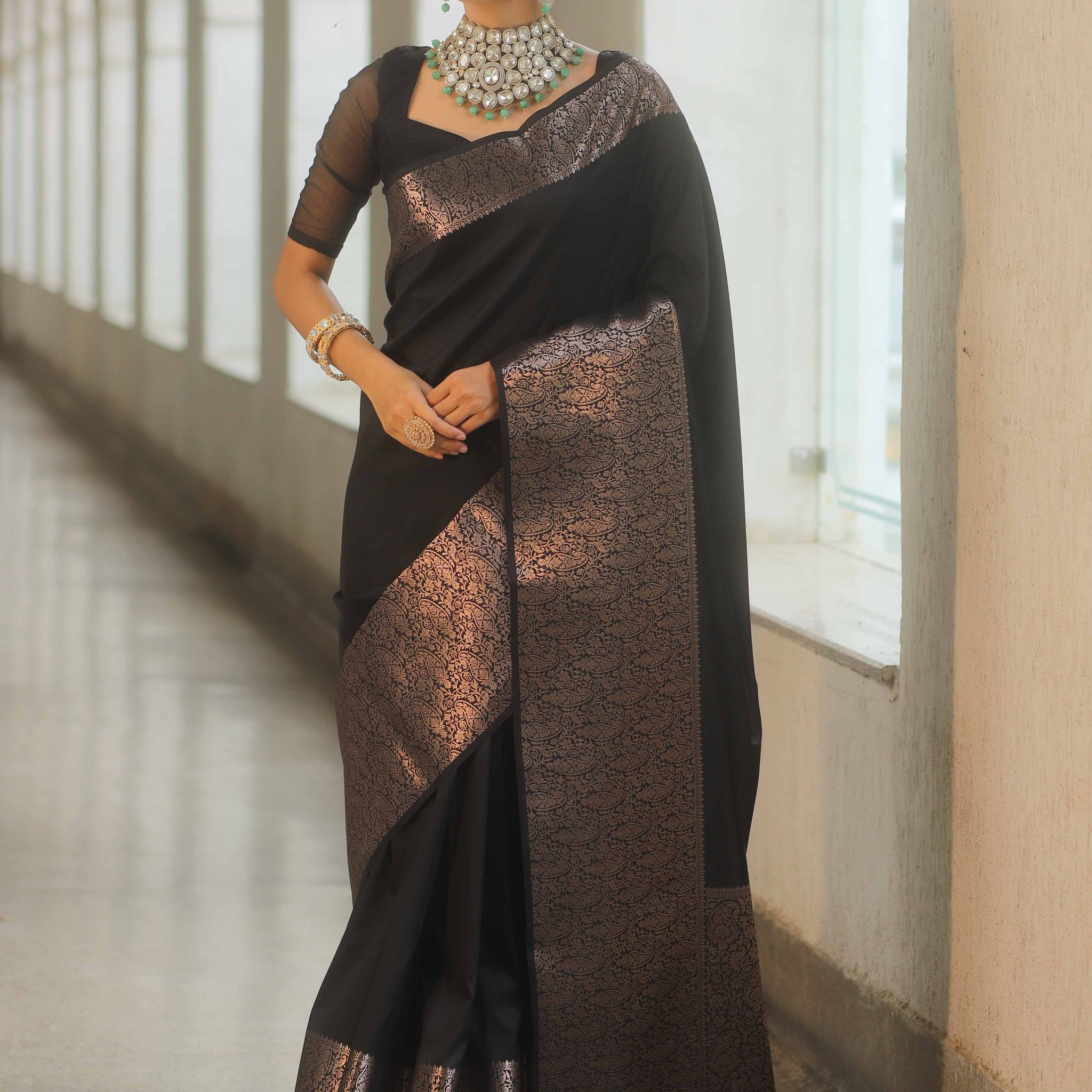 Woman wearing a black and bronze saree with jewelry indoors.
