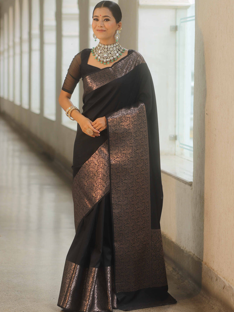 Woman wearing a black and bronze saree with jewelry indoors.