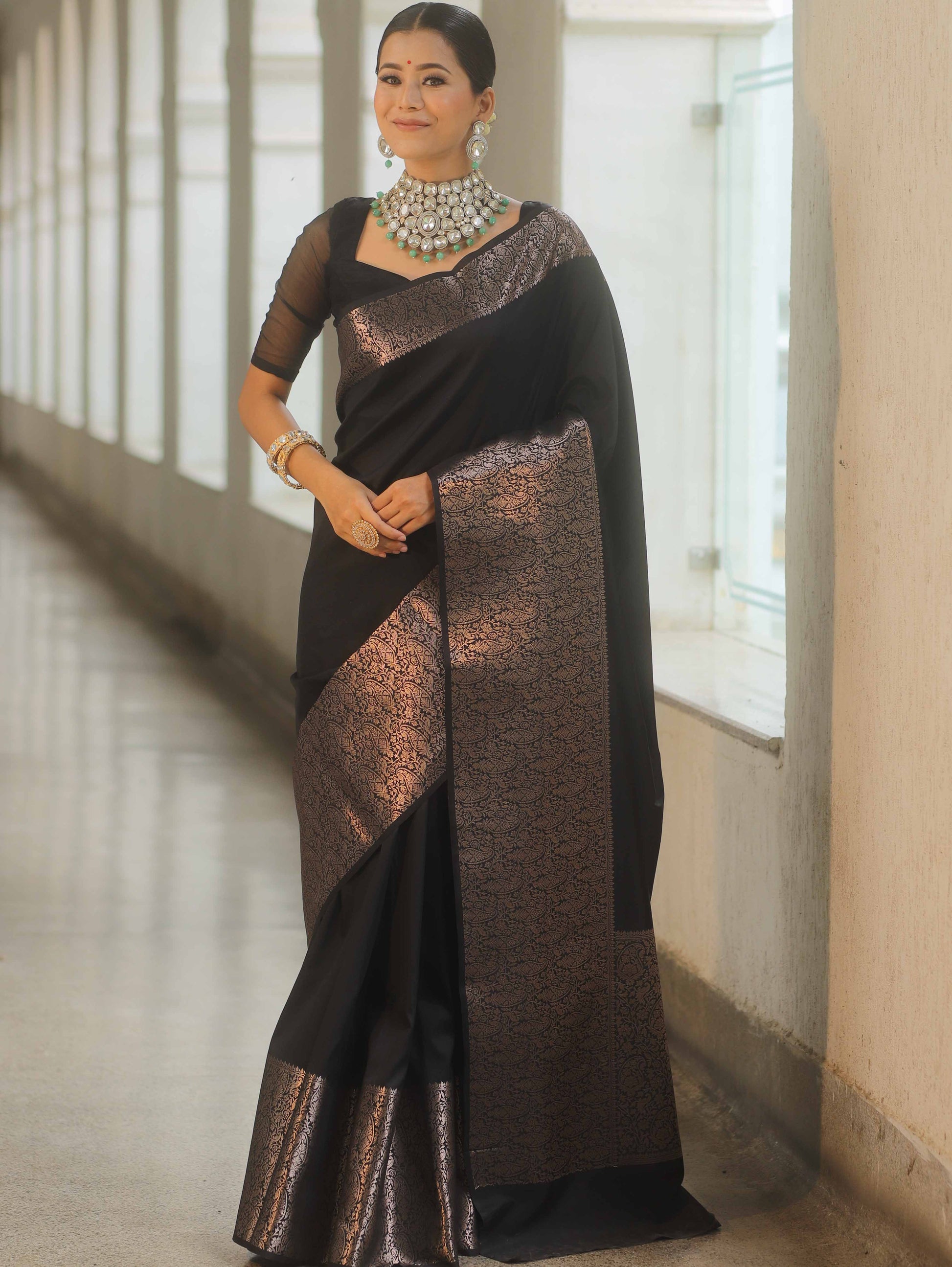 Woman wearing a black and bronze saree with jewelry indoors.