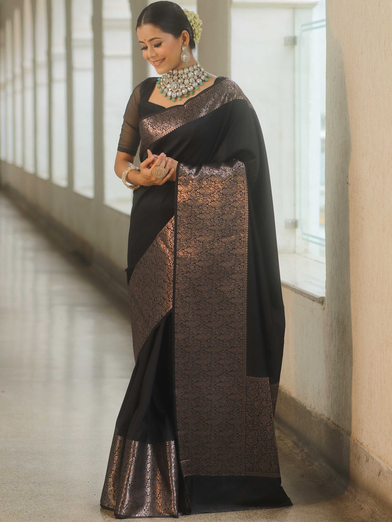 Woman wearing a black and bronze saree with jewelry indoors.