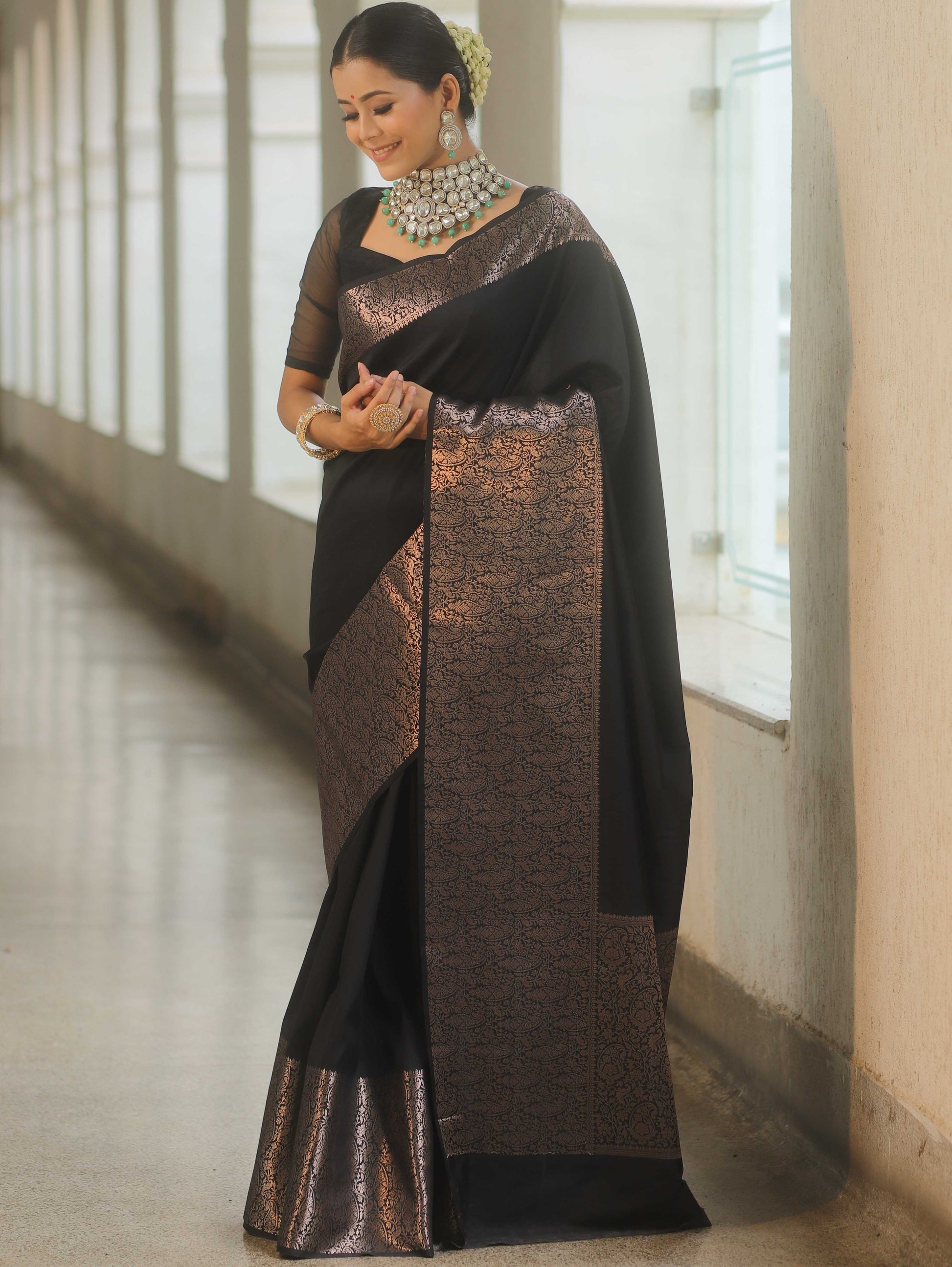 Woman wearing a black and brown saree with a white wall background