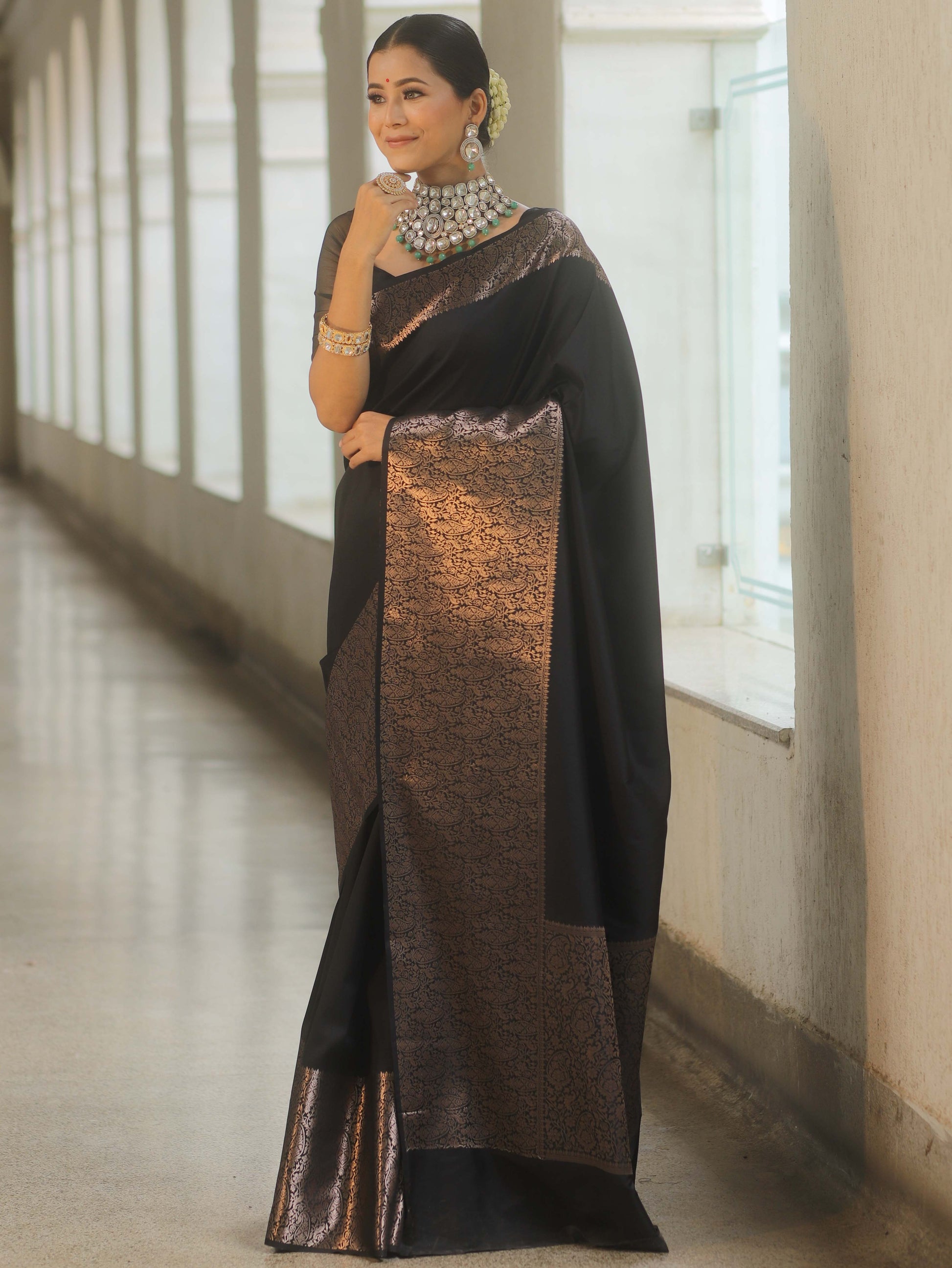 Woman wearing a black saree with a metallic border indoors.