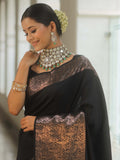 Woman wearing a black saree with intricate patterns and heavy jewelry indoors.