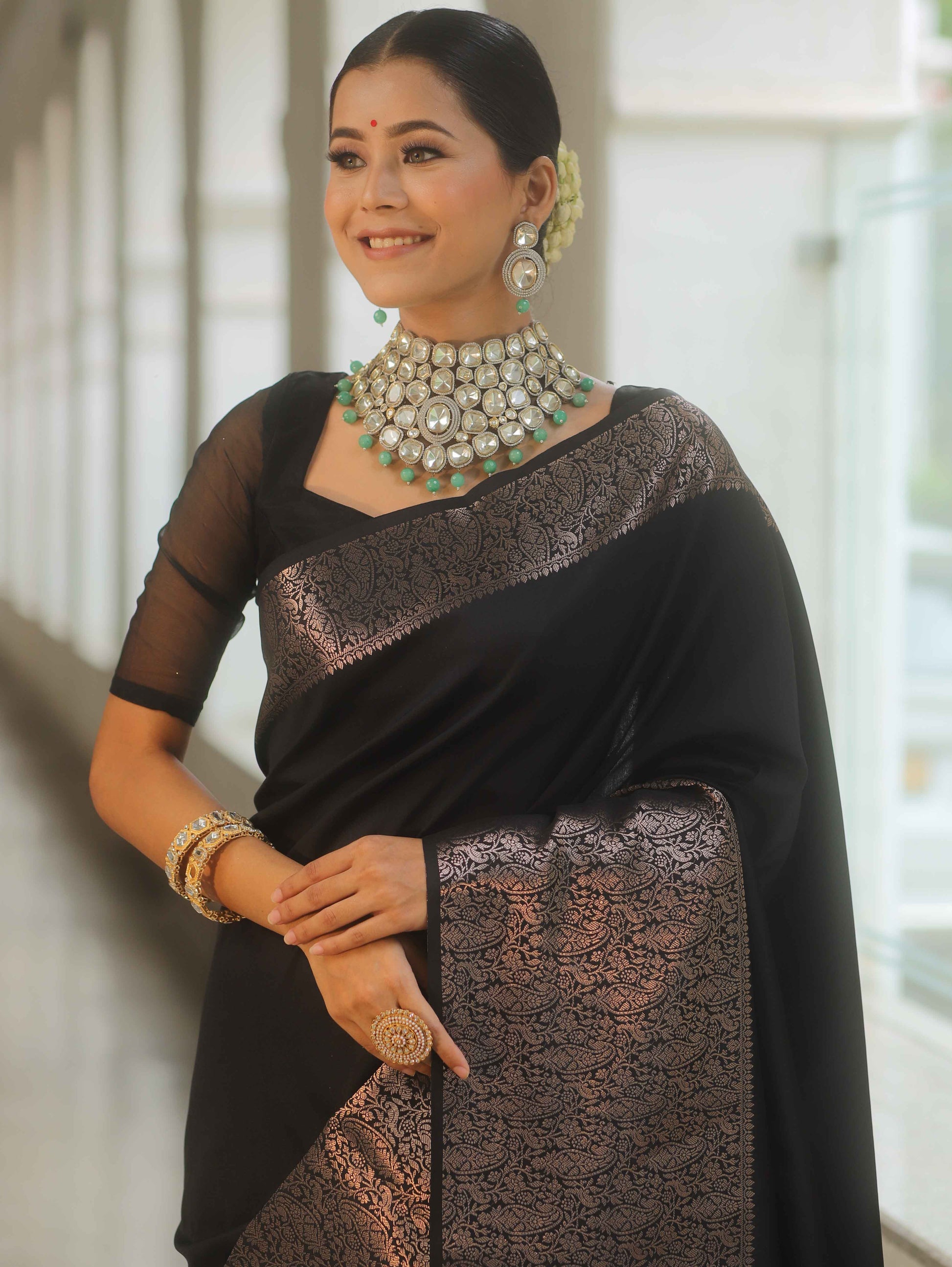 Woman wearing a black saree with silver border and jewelry indoors