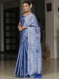 Woman wearing a blue saree with intricate patterns indoors.