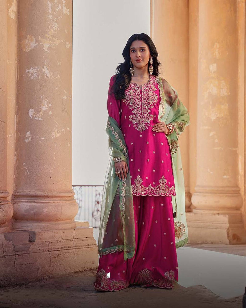 Woman in a pink and green traditional outfit standing in front of classical architecture.