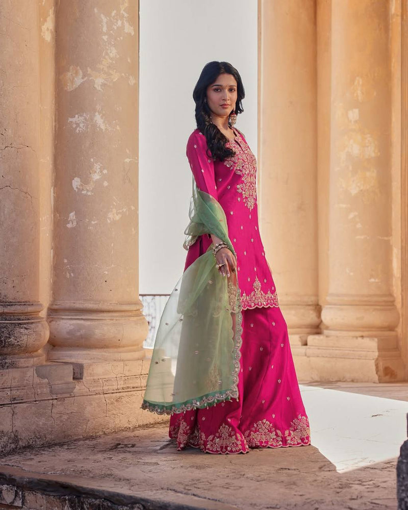 Woman in a pink and green traditional outfit standing in front of classical architecture.