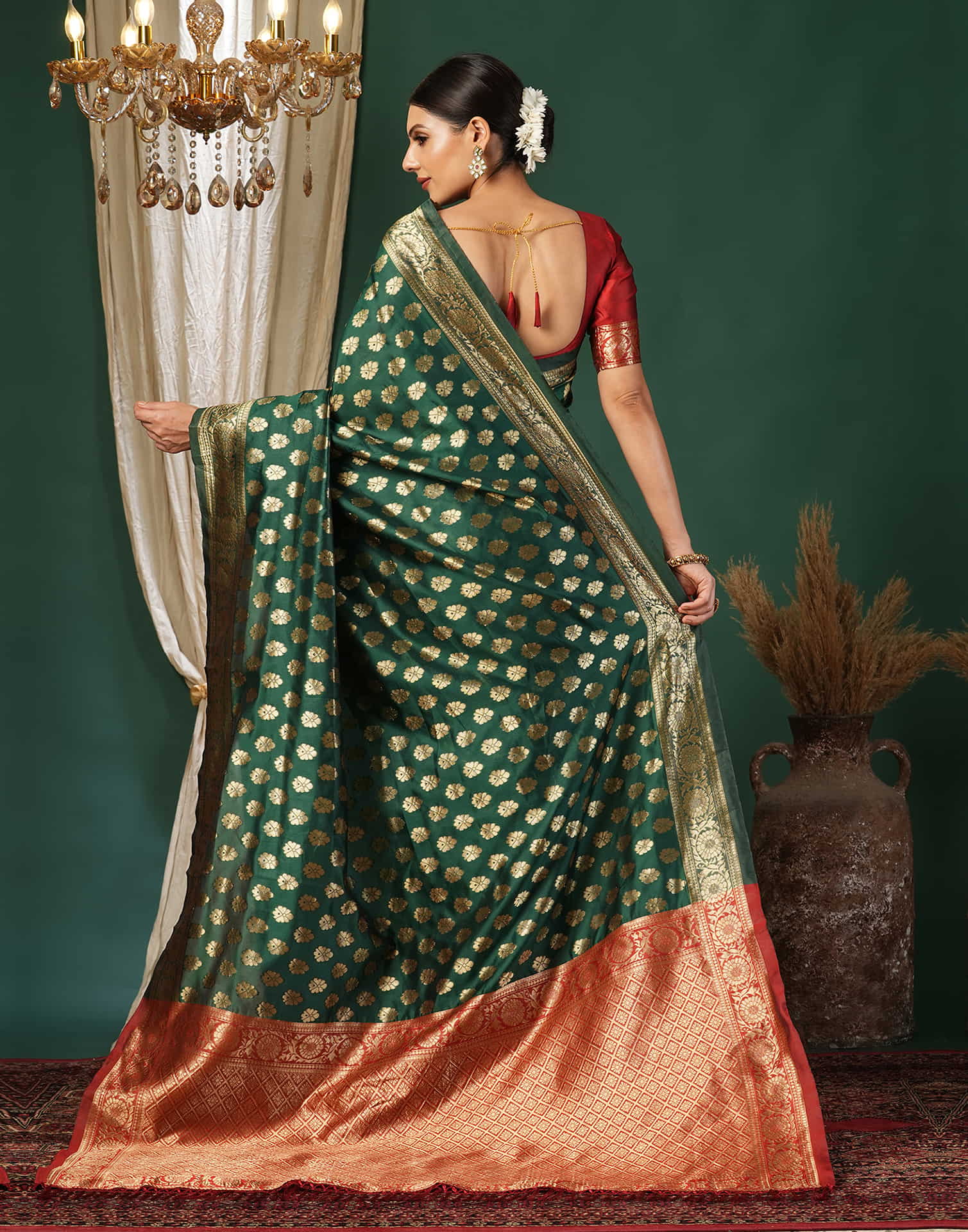 Woman wearing a green and gold saree with a chandelier and vase in the background