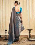 Woman wearing a blue and gray saree with a beige curtain background