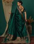 Woman in a green saree with gold details against a dark green background