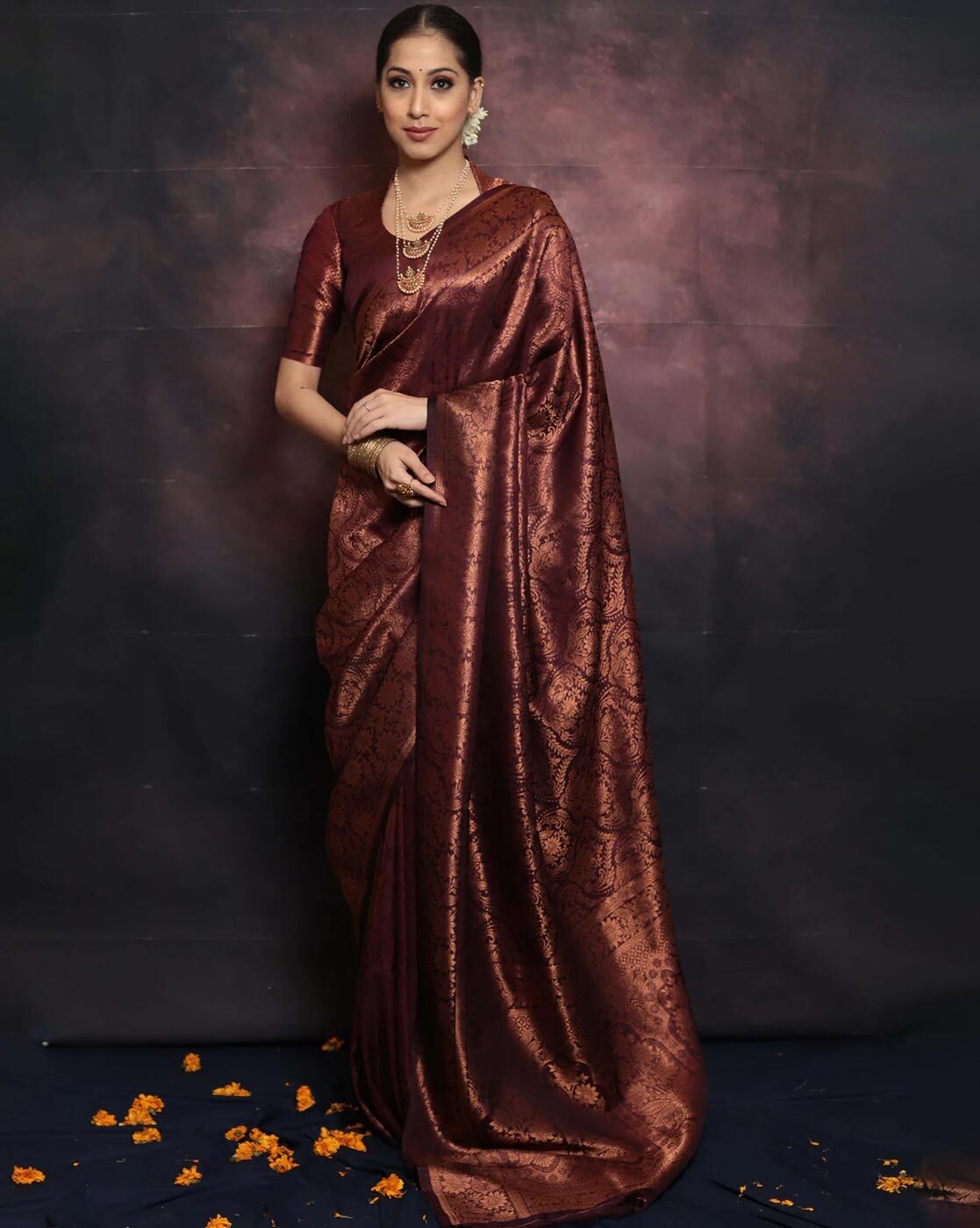 Woman wearing a maroon saree against a dark background