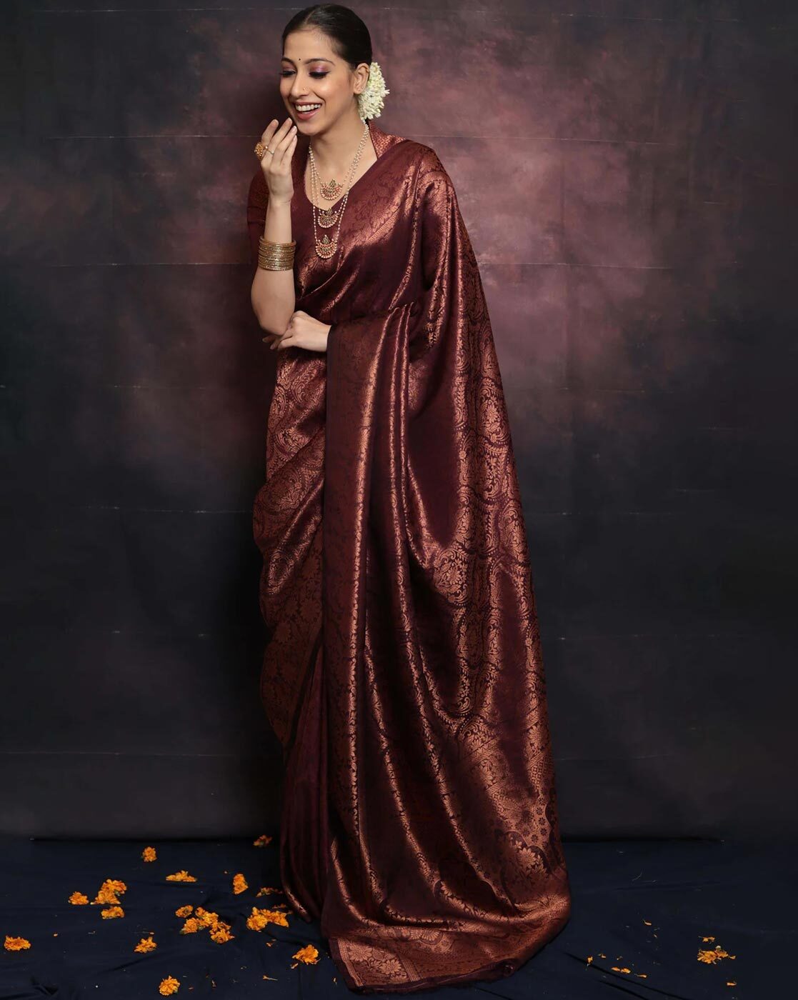Woman in a maroon saree with jewelry against a dark background