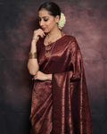 Woman wearing a maroon saree with gold patterns against a dark background