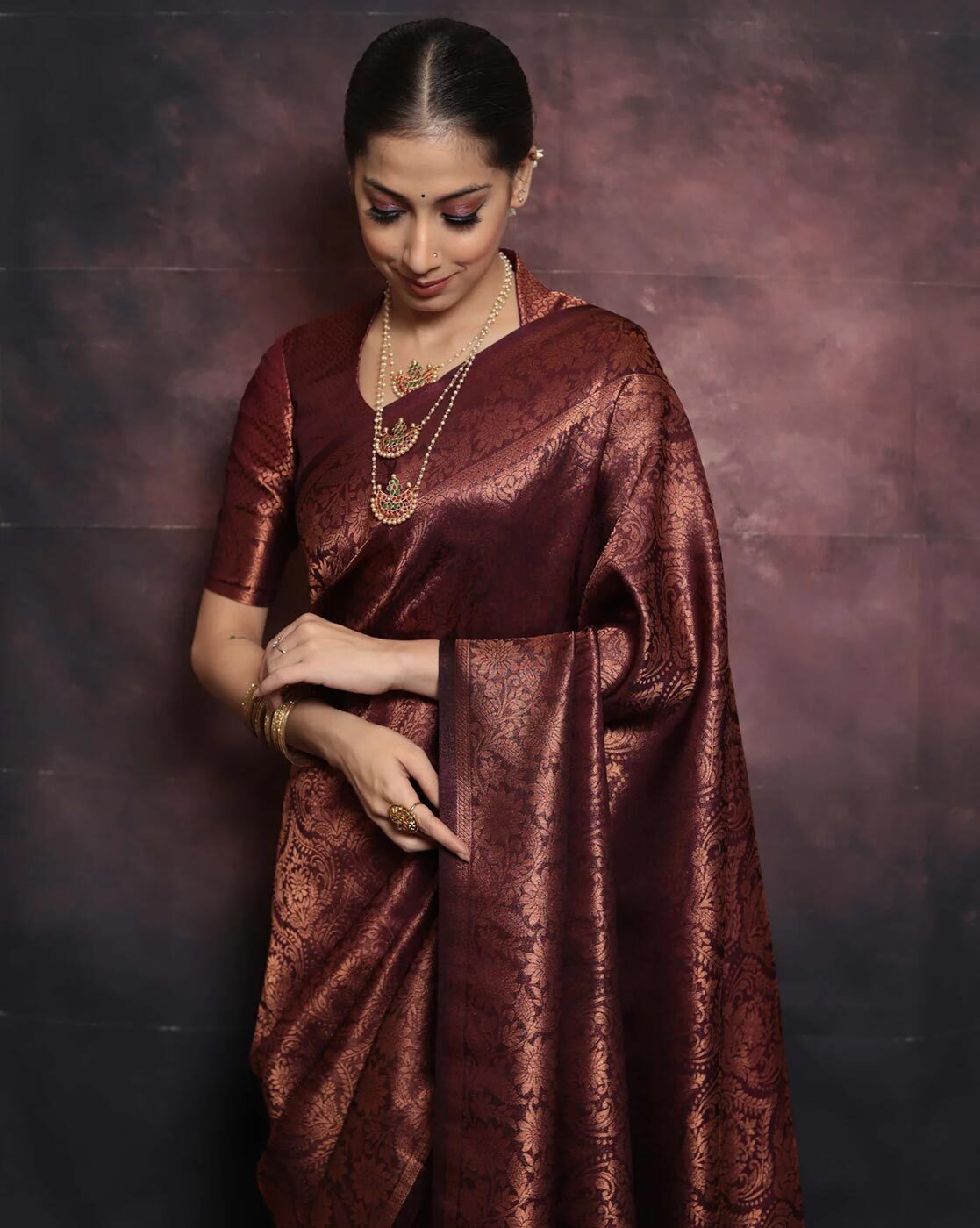 Woman wearing a maroon saree with a textured pattern against a dark background