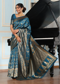 Woman in a blue and silver saree standing next to a grand piano in a room with light blue walls.