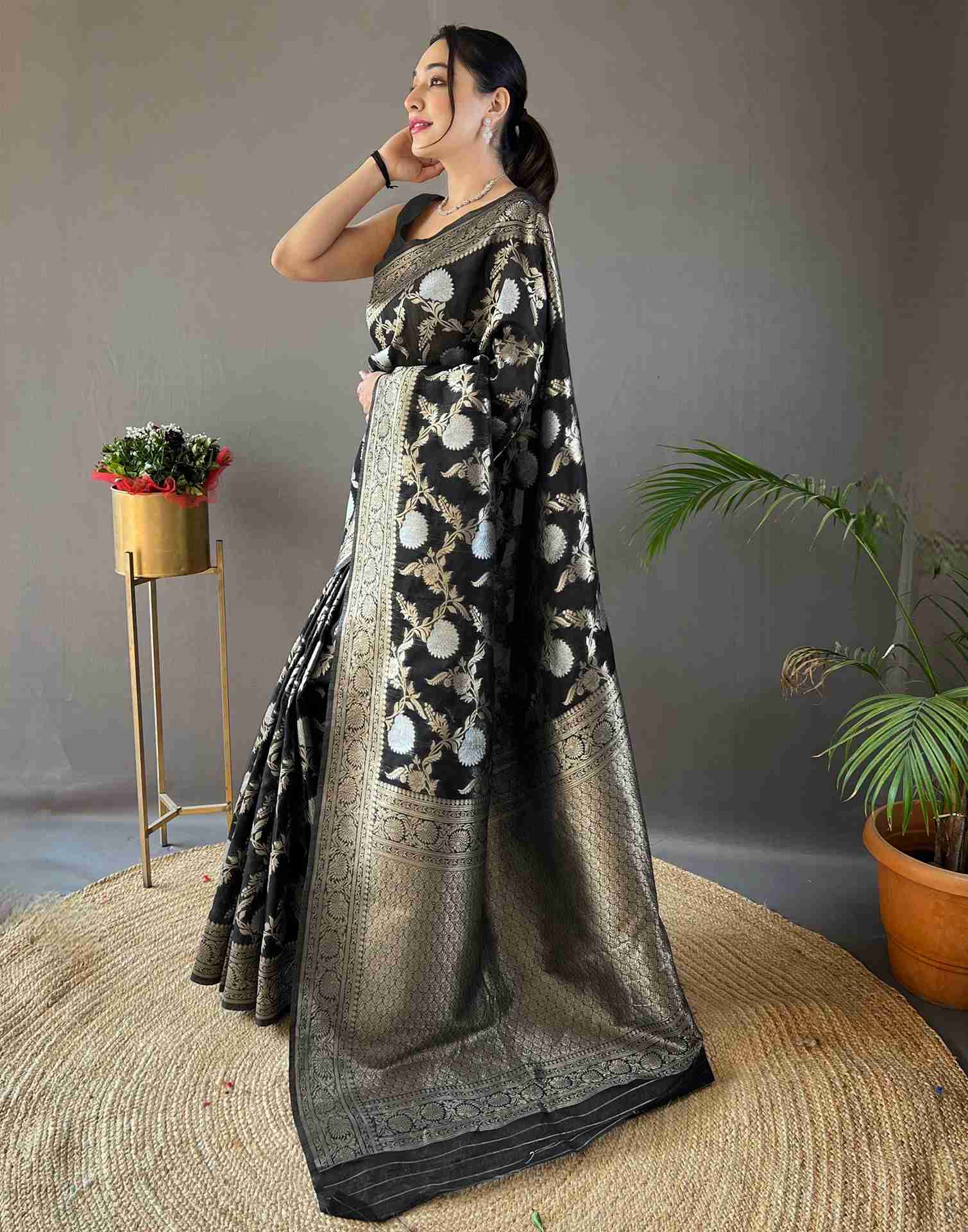 Woman wearing a black and gold saree with a patterned design, standing against a gray background.