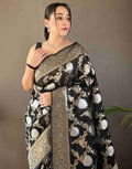 Woman wearing a black saree with floral patterns against a plain background