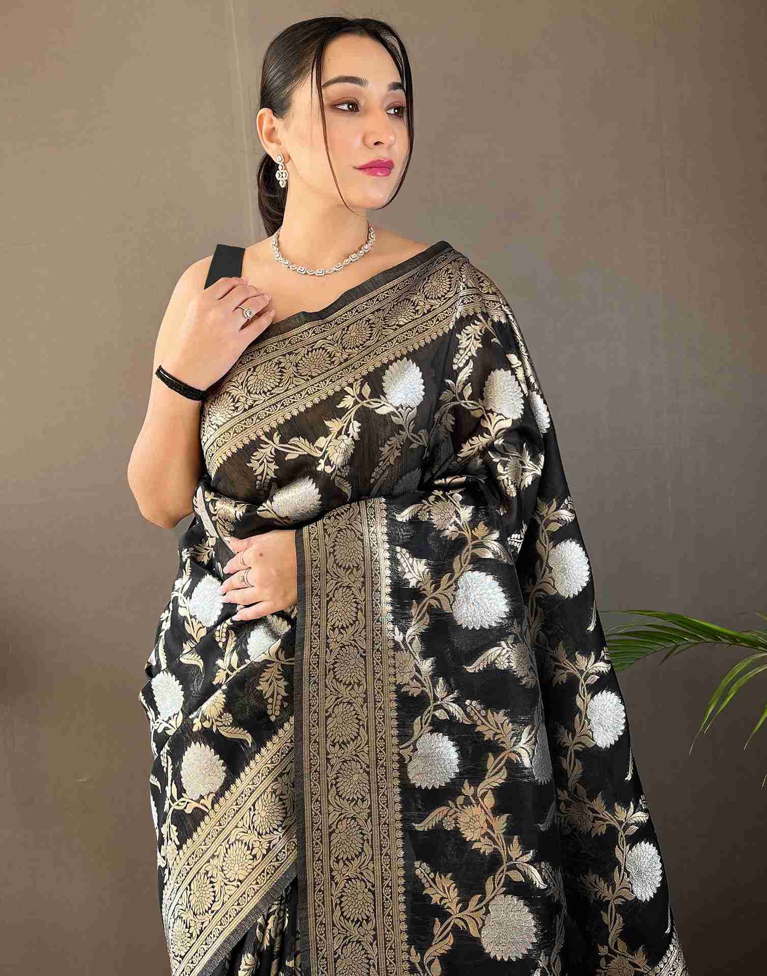 Woman wearing a black saree with floral patterns against a plain background