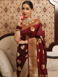 Woman in a traditional maroon saree with gold patterns against an ornate wall.