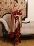 Woman in a red and gold saree standing in front of a decorative wall and sofa.