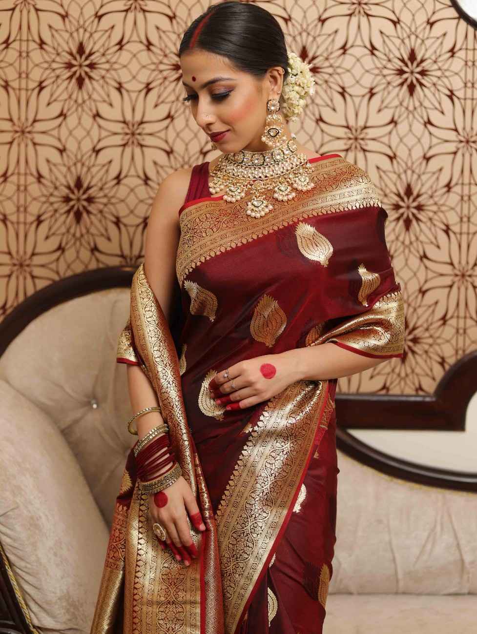 Woman in a maroon saree with gold patterns against a decorative wall.