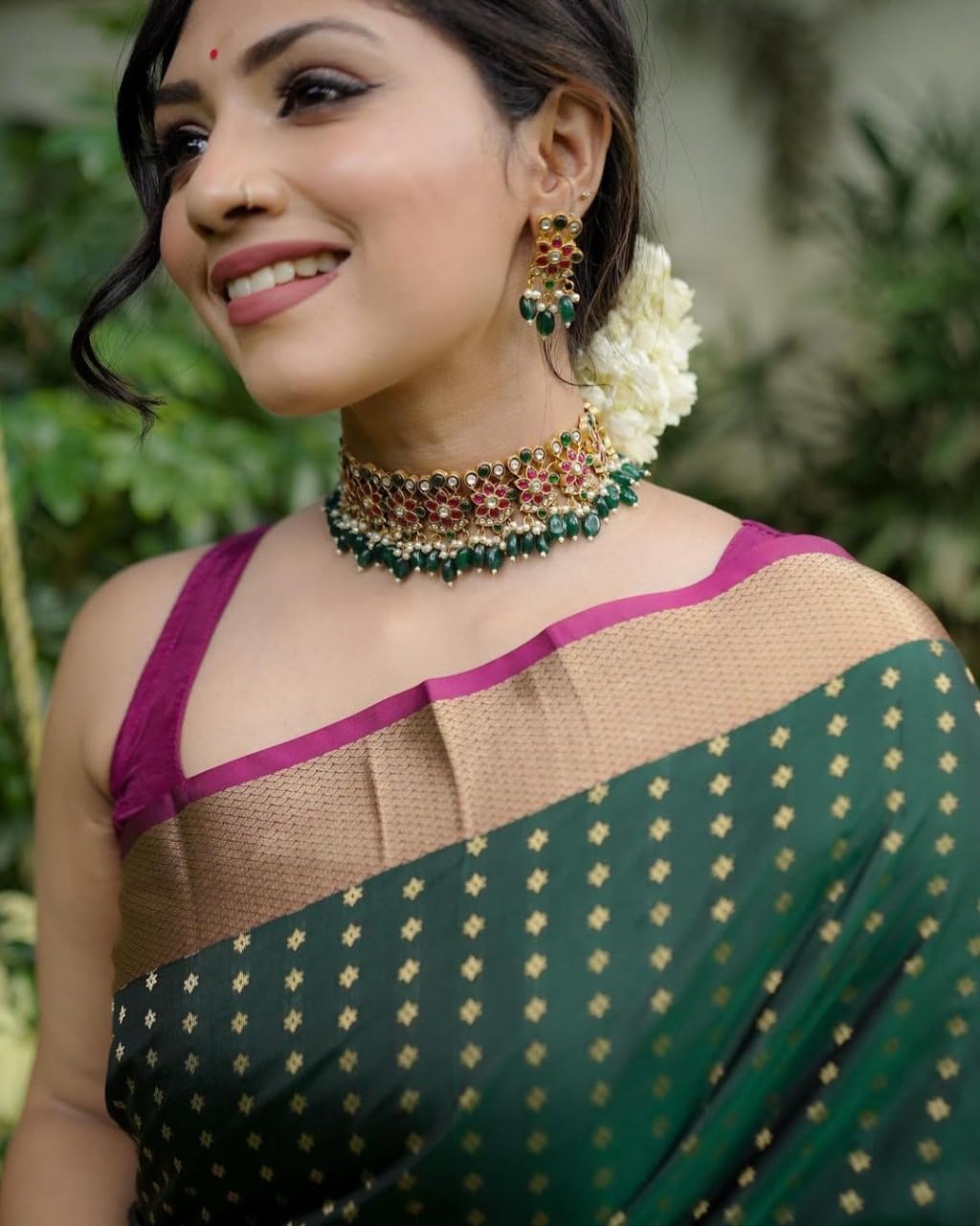 Woman wearing a green saree with a pink blouse, smiling outdoors.