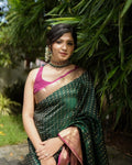 Woman in a green saree with a pink blouse standing outdoors among greenery