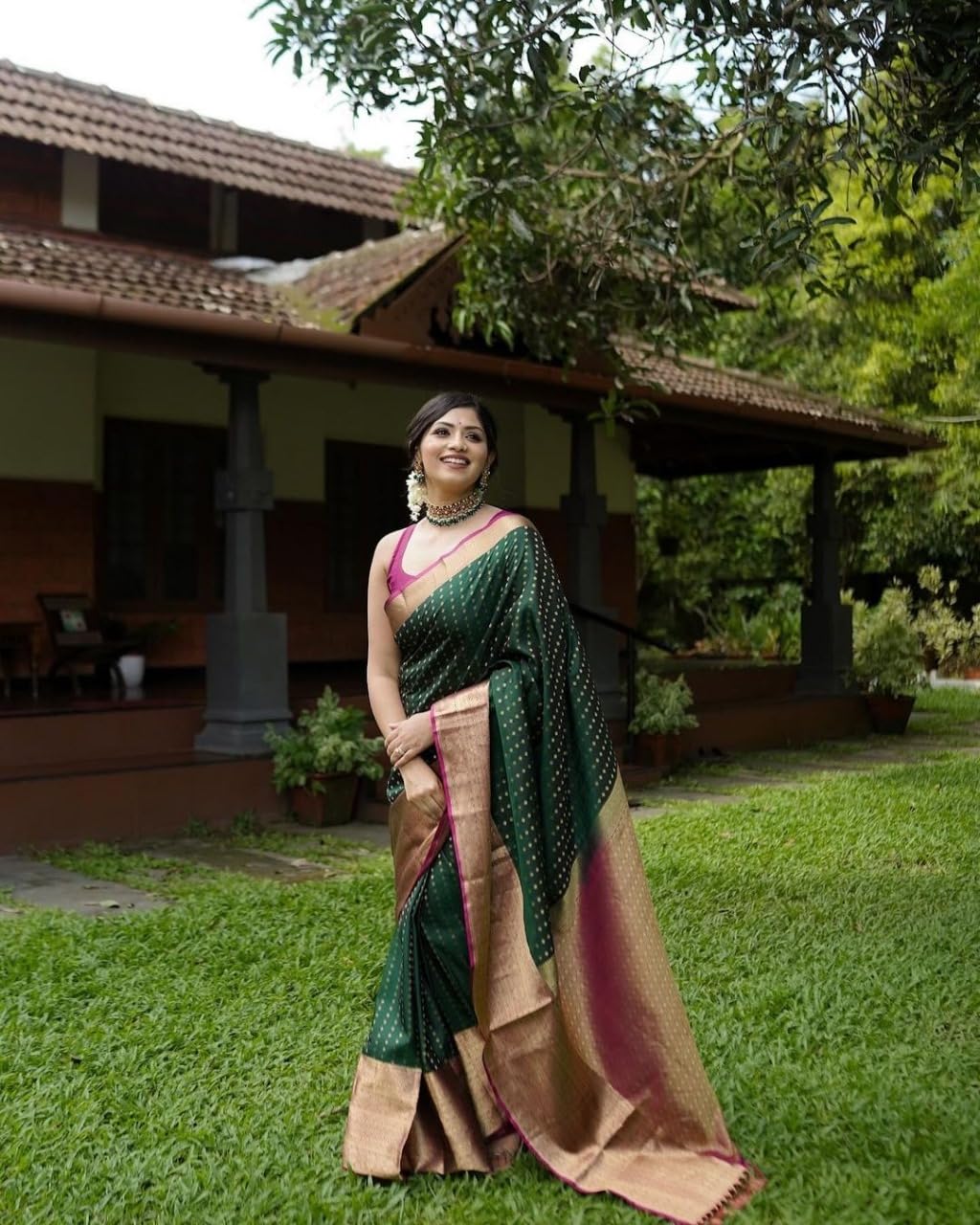 Woman in a green saree standing outdoors with a traditional building in the background