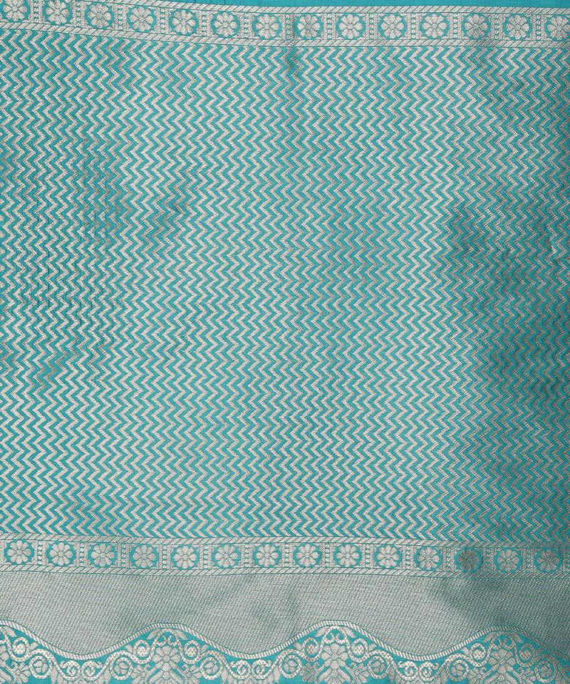 Woman wearing a teal saree with gold border on a beige background