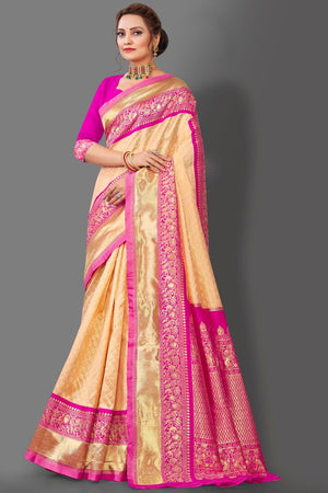Woman wearing a beige and pink saree with intricate patterns on a gray background