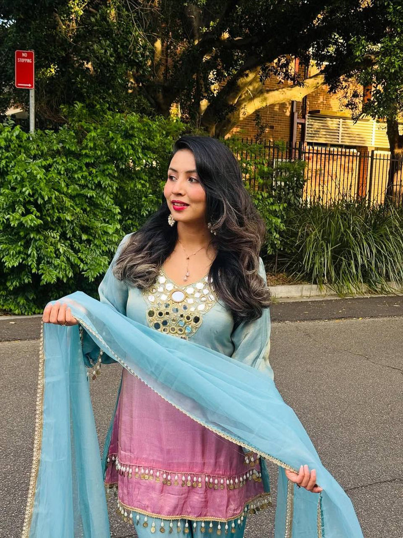 Woman in a light blue and pink traditional outfit standing in a store with 'Junkeri' branding.