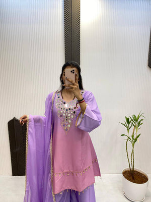 Person wearing a purple traditional outfit with a white wall and plant in the background